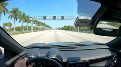 White car rental driving on a sunny Florida highway lined with tall palm trees