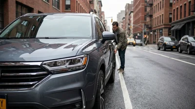 A driver inspecting a cracked windshield and flat tire on a car rental parked on a New York city street