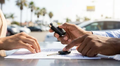 Close-up of hands inspecting a car rental key fob and spare key at a sunny pick-up lot in California