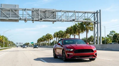 White car rental driving under an electronic toll gantry on a sunny Florida highway