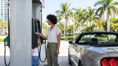 Person paying with a credit card at a gas station pump next to a car rental in Miami