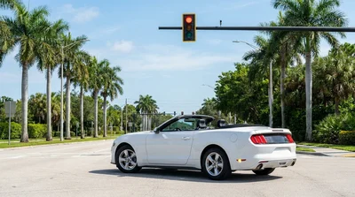White car rental stopped at a red traffic light preparing to turn right on a sunny Florida street