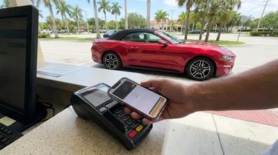Person holding a smartphone over a payment terminal at a Florida car rental desk