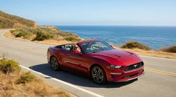 White car rental driving on a sunny coastal road overlooking the ocean in California