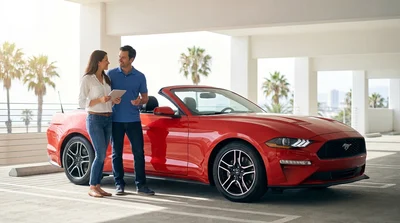 A person driving a sleek car rental along a sunny coastal highway in California