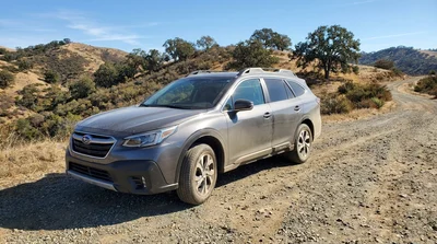 White car rental driving on a dusty unpaved road through a scenic desert landscape in California