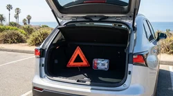 Warning triangle and first aid kit inside the open trunk of a car rental parked on a sunny road in California