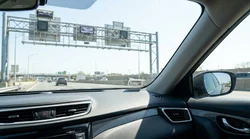 Driver in a car rental passing under an overhead cashless toll gantry on a New York highway