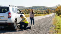 Driver inspecting a flat tire on a car rental along the side of a road in Pennsylvania