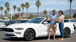 Person driving a car rental on a sunny coastal highway in California