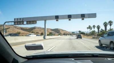 Silver car rental driving on a sunny California highway approaching a toll booth
