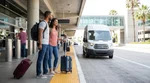 Traveler with luggage exiting a rideshare vehicle near a car hire shuttle at Los Angeles airport
