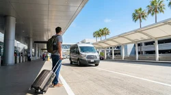 Travelers with luggage waiting for a car rental shuttle outside LAX Terminal 1 in Los Angeles