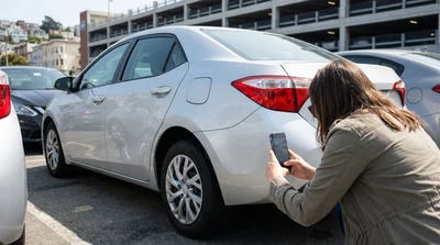 Person taking a smartphone photo of a car rental vehicle in a San Francisco parking garage