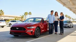 Couple driving a white convertible car hire along a scenic coastal road in California