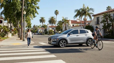 Silver car rental driving past a cyclist and pedestrians on a sunny California road