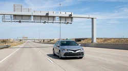 Driver in a car rental passing under an electronic toll gantry on a Texas highway