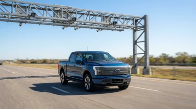 A silver car rental passing under an overhead toll gantry on a sunny Texas highway