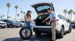 Driver checking a spare wheel in the trunk of a car rental parked on a California coastal road