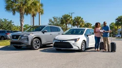 White compact car rental parked next to tall palm trees on a sunny beach in Florida