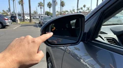 Driver checking the side mirror of a car rental parked on a sunny street in California