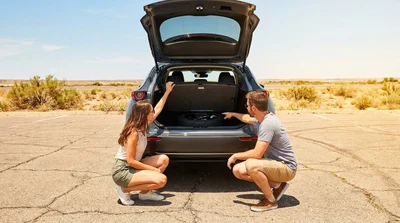 Person checking the spare tire in the open trunk of a car rental parked on a sunny Texas highway
