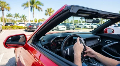Person checking the dashboard odometer of a car rental parked under palm trees in Florida