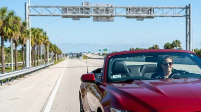 White car rental passing under an electronic toll gantry on a sunny highway in Florida
