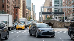 A driver in a car rental waiting in heavy traffic on a busy street surrounded by tall buildings in New York