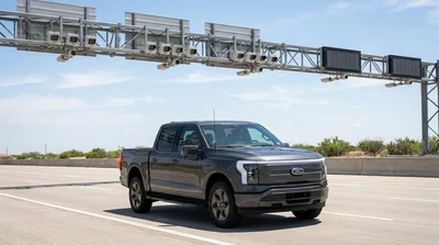 Silver car rental driving under an electronic toll gantry on a sunny Texas highway