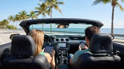 Person using a smartphone inside a car rental parked near a sunny beach and palm trees in Florida