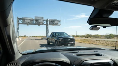 A modern car rental driving under an electronic toll gantry on a Texas highway