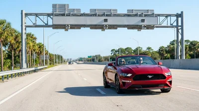 White car hire passing under an electronic toll gantry on a bright Florida highway