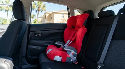 Young child buckled into a booster seat in the back of a Florida car rental with palm trees outside the window