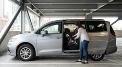 Parent installing a child safety seat in the back of a car rental parked on a New York street