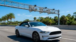 Silver car rental driving on a multi-lane Florida highway passing under a toll gantry