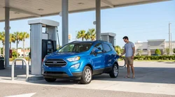 Person pumping gas into a white car rental at a sunny gas station in Orlando