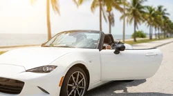Person driving a car rental along a sunny coastal highway with palm trees in Florida