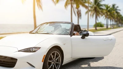 Person driving a car rental along a sunny coastal highway with palm trees in Florida