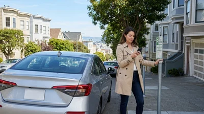 Person using a smartphone next to a car rental parked on a steep San Francisco street