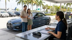 A sleek white convertible parked under palm trees at a sunny Miami car rental lot