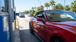 White car rental approaching an electronic toll plaza on a sunny palm-lined highway in Florida