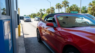 White car rental approaching an electronic toll plaza on a sunny palm-lined highway in Florida