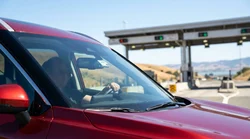 White car rental driving under an electronic toll plaza on a sunny highway in San Francisco