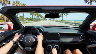 Driver behind the steering wheel of a car rental cruising down a sunny highway in Florida