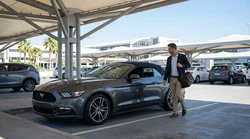 Traveler pulling luggage past parked vehicles in a Los Angeles car rental parking lot
