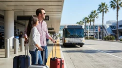 Travelers with luggage waiting for a Hola car hire shuttle bus outside Terminal 4 in Los Angeles