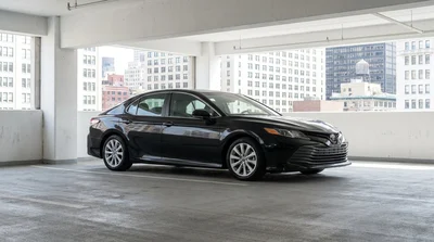 A silver car hire driving past tall skyscrapers on a sunny street in New York