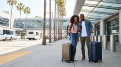 Travelers with luggage waiting for a car hire shuttle outside Terminal 7 in Los Angeles
