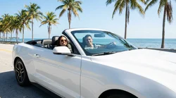 Young adult driving a convertible car rental along a sunny palm-lined street in Miami